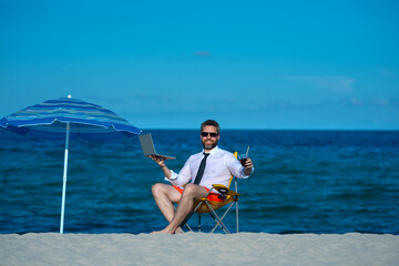 Wall Mural - Business vacation. Handsome businessman on summer vacation. Businessman rest on sea beach holding laptop. Summer business. Freelancer on summer sea beach. Summer weekend and remote freelance work.