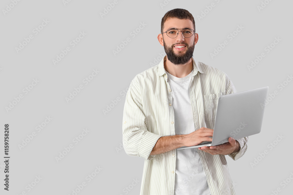 Young bearded man using laptop on light background