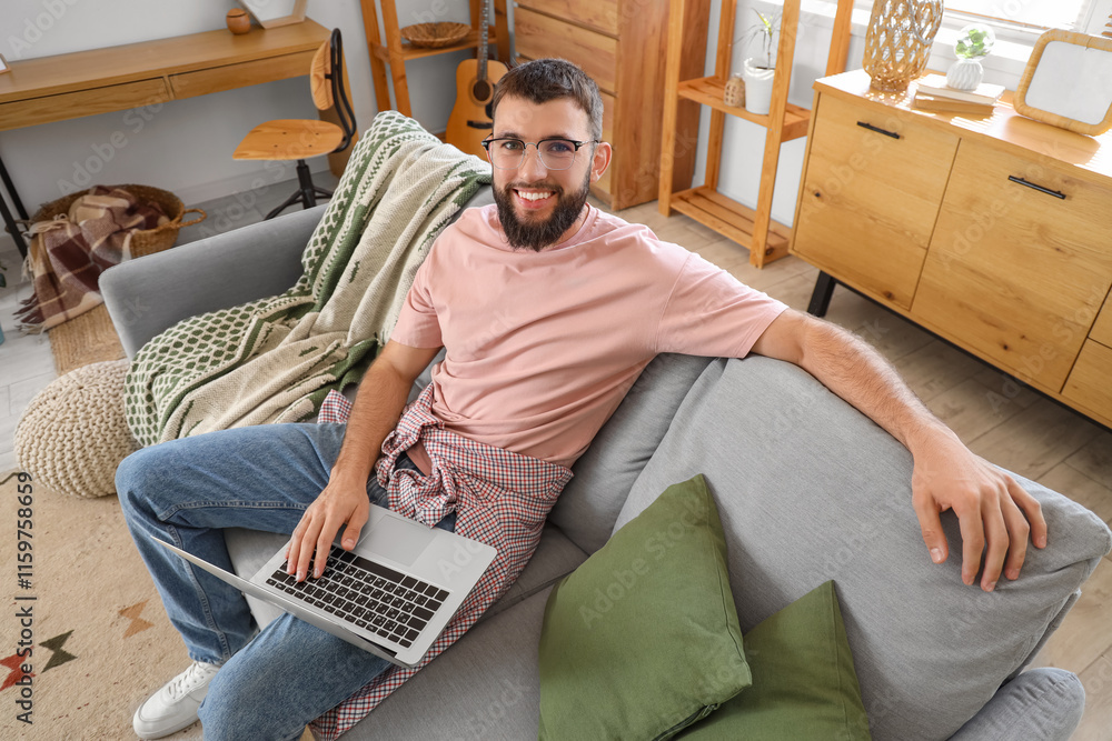 Young bearded man using laptop on sofa at home