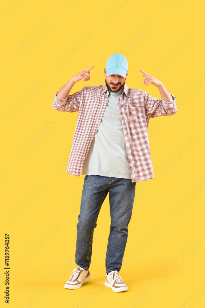 Young man pointing at cap on yellow background