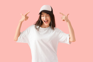 Wall Mural - Beautiful young woman in white t-shirt pointing at cap on pink background