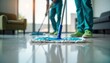© Maryna - Two people clean tiled floor with mop, cloth. Wear teal uniforms, use mops to maintain cleanliness in modern indoor corridor hall. Daily chore keeps place hygienic, sterile. Floor shines after clean.