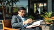 © Chalermrach - Smart Asian businessman sitting outside, clad in a tailored suit, enjoying a cup of coffee and reading a book at a cafe table, coffee, cafe