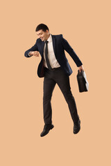 Wall Mural - Jumping businessman with briefcase looking at wristwatch on beige background. Time management concept