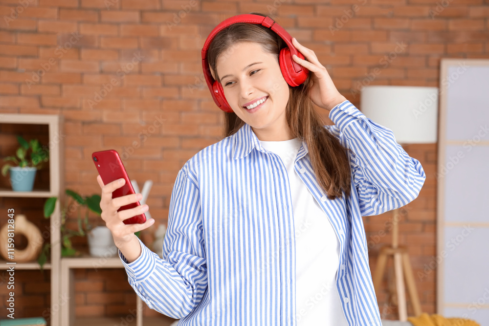 Smiling young woman in headphones using mobile phone at home