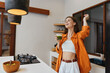 © SHOTPRIME STUDIO - Happy young woman celebrating healthy lifestyle with green smoothie in modern kitchen, wearing orange shirt and white top, enjoying vibrant atmosphere and fresh colors