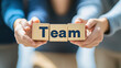© 沈军 贡 - Team members holding wooden blocks with the word 'Team' on them, close-up of hands and text, blurred background