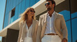 © Anastasiia Havelia - Photo of an attractive young couple walking and smiling, wearing beige blazer suits with white trousers, sunglasses, in front of a modern office building, on a summer day, taken fr