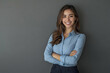 © Fazal - Portrait of a businesswoman wearing a blue shirt and dark trousers, smiling while standing with her arms crossed against a grey background, captured in professional lighting.