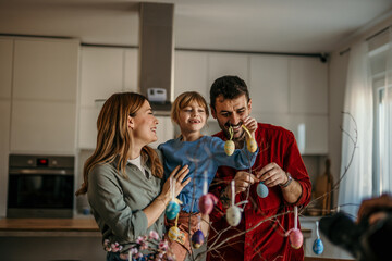 Wall Mural - Parents and children smiling while decorating eggs with vibrant paints and glitter for Easter.