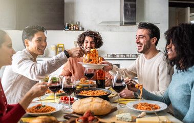 group of smiling friends sharing spaghetti and wine at a kitchen table. diverse young adults enjoyin