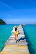 © Fokke Baarssen - A traveler in a vibrant swimsuit walks barefoot on a rustic wooden pier, surrounded by clear turquoise waters and a breathtaking sky. The tropical paradise invites relaxation and exploration.
