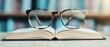 © thanawat - Emotional Value concept. Glasses resting on an open book with blurred background of shelves.