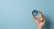 © Paintbrush - A hand holds a blue smiling emoji against a plain light blue background, symbolizing happiness.