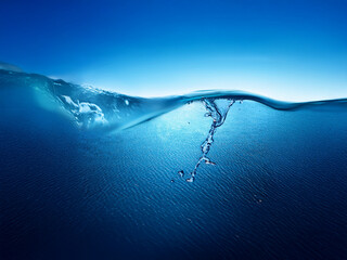 Poster - A serene underwater scene.  The surface of the water is gently curved, showing both above and below the waterline.  Bubbles rise from the depths in a swirling motion. The deep blue hues create a sense