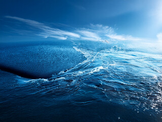 Poster - A powerful ocean wave crests, its deep blue surface glistening under a bright sky.  Whitecaps and spray add texture to the scene, conveying power and serenity.