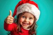 © Alla - A young girl wearing a Santa hat gives a thumbs up in a cheerful mood