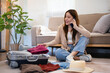 © Fahng - Happy young woman sitting near open suitcase with clothes, speaking on smartphone, booking travel tour, making hotel reservation or buying tickets on phone from home.