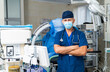 © Vadim - Health pro in a modern hospital. A male doctor stands confidently in a hospital room, wearing scrubs and a mask, surrounded by medical equipment.