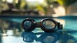 © Imam - A pair of black swimming goggles rests on the edge of an outdoor swimming pool.