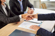 © Studio Romantic - Cropped photo of business people sitting at the desk on workplace in office shaking hands with a colleague reaching agreement making a good deal or signing a contract. Business people at work.