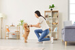 © Studio Romantic - Smiling young woman training her maltipoo dog in living room, enjoying leisure with pet. Cheerful female pet owner playing with her small puppy, teaching to do actions and follow instructions at home.