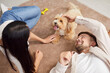 © Studio Romantic - Young loving couple, happy family owners playing with cute pet puppy at home, spouses enjoy time together having fun with small pedigreed dog on carpet, indoor leisure activity in new living room