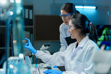 Wall Mural - two scientists wearing lab coats and safety glasses analyzing data on computer in laboratory at nigh