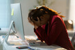 ©  NCST Studio - Young businesswoman holding her head in hands, suffering from headache or stress, working on computer in office at night