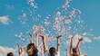 © Довидович Михаил - Friends celebrating joyfully outdoors, throwing colorful confetti under a blue sky. Arms raised in excitement, surrounded by a cheerful atmosphere