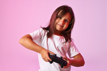 Cute little girl playing video game with controller on pink background