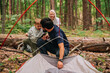 © Julia Suhareva - a man puts up a tent in the forest with him, his family is a young wife and little son. they are happily relaxing on a hike