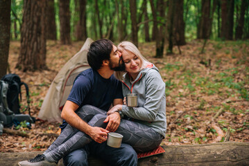 a guy and a girl in love on a hike in the forest with a tent, hugging and drinking tea