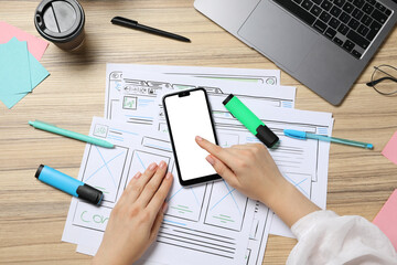 Wall Mural - website designer using smartphone at wooden table with wireframes and laptop, top view