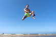 © Juan Pedro Peña - Hombre luchador de kick boxing dando una patada en el aire, un día soleado con cielo azul de verano en la playa haciendo deporte.