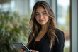 © VinakMotion - A confident Hispanic businesswoman holding a tablet, standing in a sunlit modern office. Her professional attire and warm smile exude executive presence