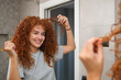 © Cavan Images - Young woman styling her beautiful curly red hair in the mirror