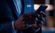 © mediavn - Close-up of a businessman in a suit holding and using a smartphone, captured in dim lighting with a professional tone.