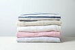 © Sunlight - Stack of perfectly folded clothing items. Pile of different pastel color shirts, sweaters and other garments on white background. Close up, copy space
