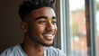 © reddish - Young man smiles while looking out the window in a cozy setting