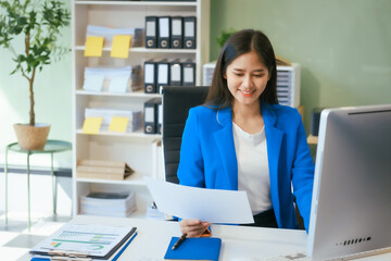 An Asian businesswoman works at her desk in a modern office, smiling while using a tablet to review financial analysis reports, manage accounting tasks, and oversee banking and loan documentation