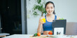 © NanSan - A happy Asian woman in sportswear sits on a sofa at a table, enjoying a salad bowl, fruits, fresh vegetables, orange juice, and energy supplements after a home fitness workout