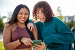 © Paula - Two young women laughing while looking at a smartphone outdoors