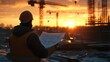 © tanongsak - Construction worker analyzing plans at sunset on a job site industrial environment perspective on project development