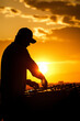 © tynza - Artistic silhouette of a DJ performing against a dramatic sunset at an outdoor music festival.