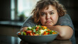 © aciddreamStudio - A sad overweight woman aged 34,, with a bowl of salad in front of her, in the kitchen