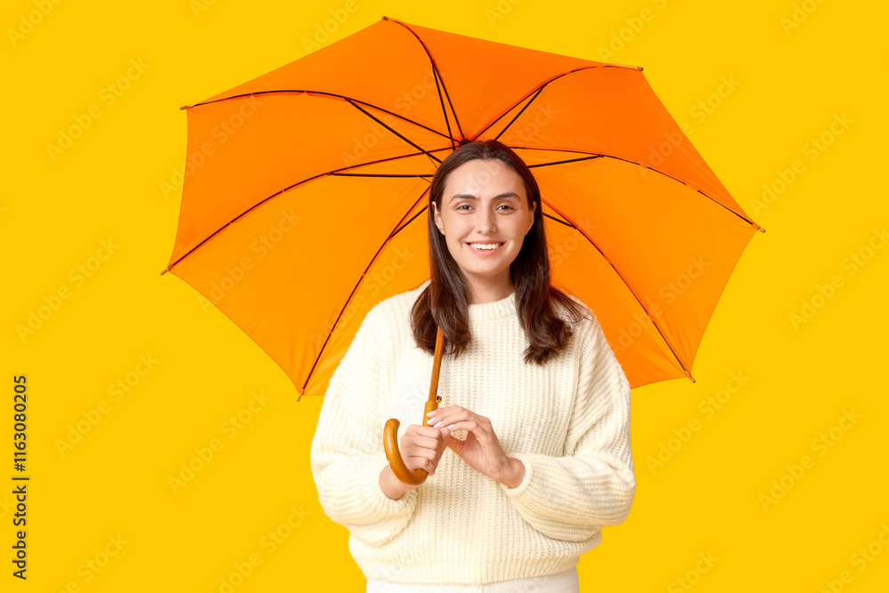 Happy young woman with umbrella on yellow background