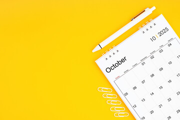 October 2025, Monthly desk calendar for 2025 year and pen with paper clips on yellow color background.