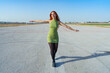 © Juan Pedro Peña - Mujer con con los brazos abiertos en una pista de aterrizaje de un aeropuerto soñando despierta que ya esta volando hacia su destino un día soleado con cielo azul.