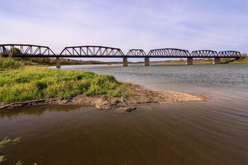 Wall Mural - A bridge spans a river with a green grassy bank